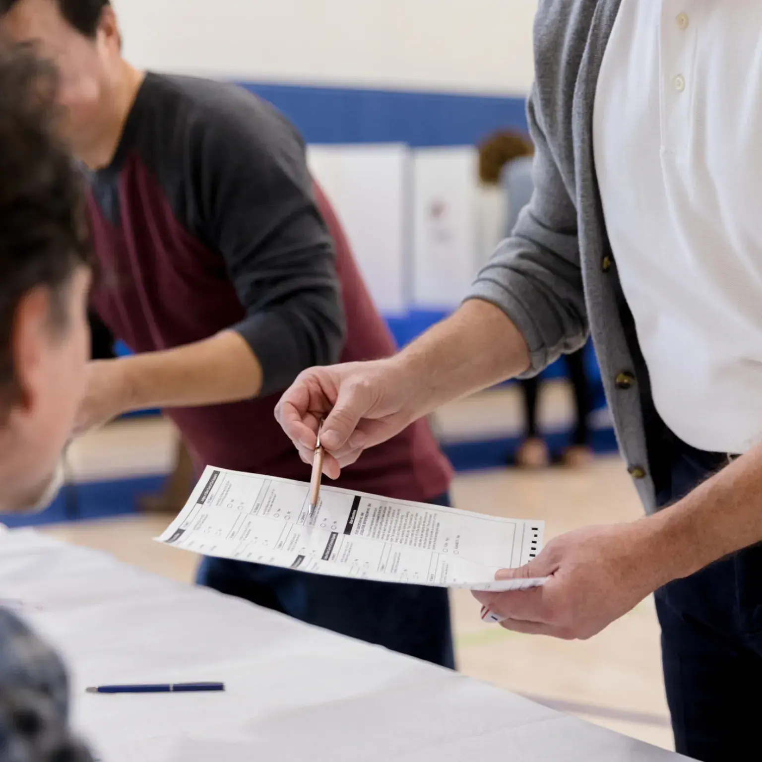 Person standing and reviewing a ballot in the background as a person sits in the foreground.